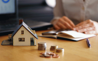 Maison miniature et pièces de monnaies posées sur un bureau (c) Freepik